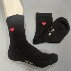 Detailed view of black merino wool socks with red heart embroidery and woven text detail.