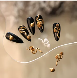 Nahaufnahme von 3D-Gold-Schlangen- und Rosen-Anhängern auf schwarzen Stiletto-Nägeln