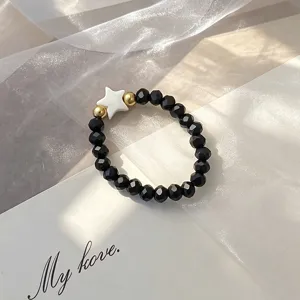 Close-up of a Bohemian elastic beaded ring with black faceted beads and a white shell star