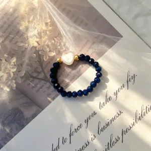 Macro detail of a navy blue crystal beaded elastic ring with a white shell heart charm