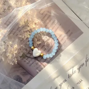 Close-up view of a light blue beaded elastic ring featuring a white shell heart charm.