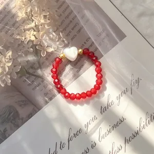 Close-up of a red crystal beaded ring featuring a white shell heart and golden accents.