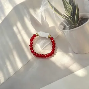 Macro view of red faceted glass beads and white shell fish charm on elastic ring