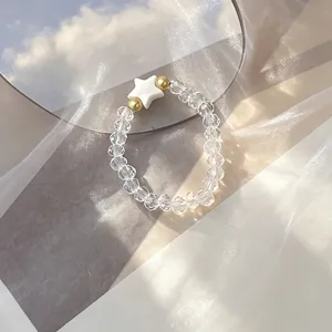 Close-up of clear glass beaded ring with white shell star on dreamy fabric background.