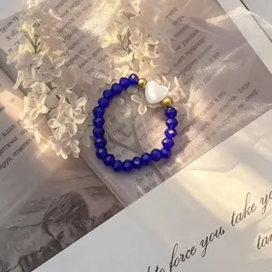 Close-up of a blue crystal bead ring with a white shell heart charm on vintage paper.
