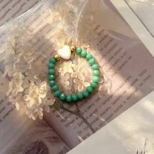 Close-up of green crystal beaded elastic ring with white heart shell charm.