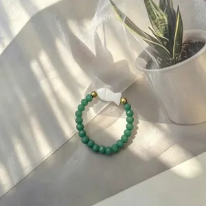 Detail view of handmade green beaded elastic ring with white fish shell charm