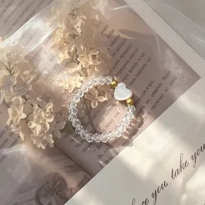 Detail of elastic ring with white shell heart and clear crystal beads on aesthetic background