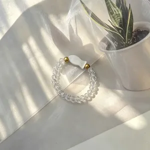 Macro view of minimalist handmade elastic beaded ring with a white shell fish charm