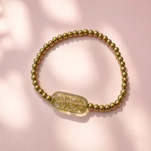Detailansicht des 18K Goldperlenarmbands mit grünem Glasanhänger und Goldgravuren
