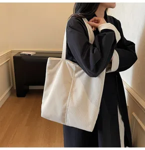 Model carrying a large white striped corduroy tote bag in a minimalist room interior