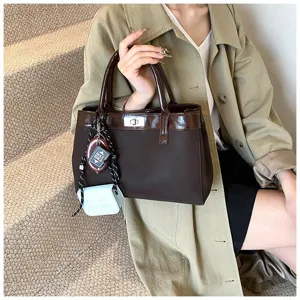 Elegant vintage brown tote bag featuring a silver metal lock and unique accessory charms on a model