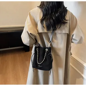 Close-up of black faux suede bucket bag with gold chain and drawstring detail on model
