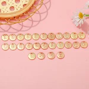 Detailed view of 26 gold A-Z alphabet charms for DIY jewelry making on pink background