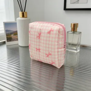 Neceser acolchado a cuadros rosa con lazos rojos sobre una elegante mesa de cristal