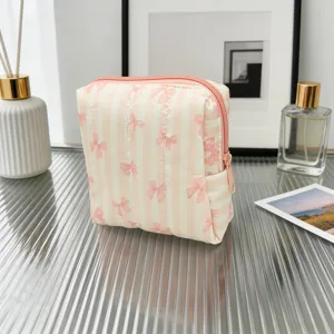 Primer plano de un neceser acolchado rosa con motivos de lazos sobre mesa de cristal