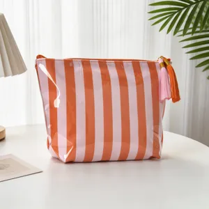 Detaillierte Ansicht der gestreiften PVC-Kosmetiktasche mit einem bunten Quastenanhänger