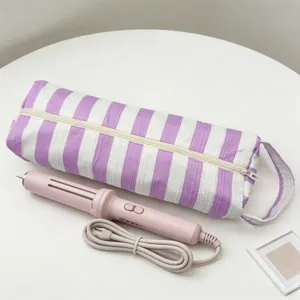 Borsa da viaggio a righe viola con arricciacapelli rosa coordinato su tavolo.