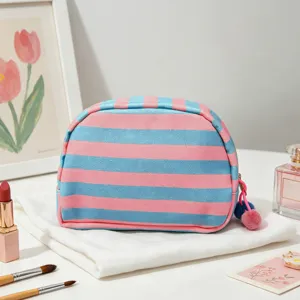 Close-up of a striped shell-shaped cosmetic bag with pink and blue colors and pom-poms