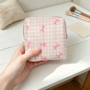 Primer plano de una mano sosteniendo una bolsa de almacenamiento rosa acolchada con lazos