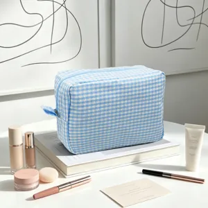 Blue and white gingham seersucker toiletry bag shown with cosmetics on a table.