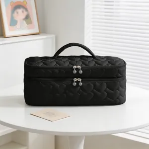 Black heart-quilted travel makeup organizer bag with double layers on a white table