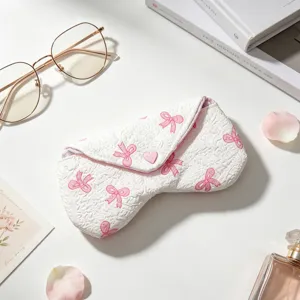 Detalle de una linda funda de tela blanca para gafas con lazos rosas y botón de corazón