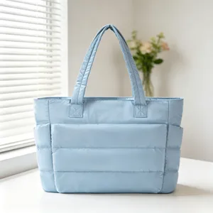 Vue détaillée d'un sac cabas matelassé bleu clair sur une table blanche dans une pièce