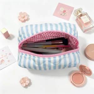 Close-up of a blue and white striped quilted makeup bag with cosmetics and brushes.