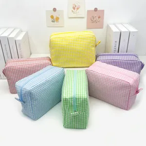 Six colorful gingham seersucker toiletry bags arranged on a white minimalist desk