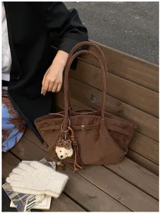 Detailansicht einer braunen Wildleder-Tragetasche mit süßem Bärenanhänger auf einer Holzbank.