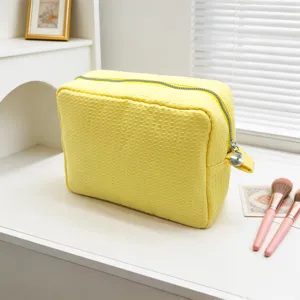 Neceser de maquillaje amarillo grande con textura de gofre en un tocador con pinceles.