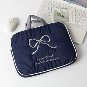 Funda para portátil azul marino con lazo bordado plateado y asa en un escritorio