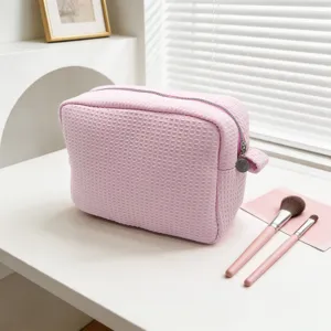 Detalle de un neceser rosa con textura de gofre y cremallera sobre mesa blanca