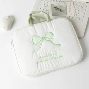 Detalle de una funda acolchada blanca para portátil con un lazo bordado verde decorativo