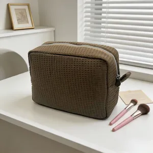 Detalle de un neceser marrón con textura de gofre en un tocador blanco con brochas