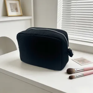 Neceser negro grande con textura de gofre y brochas de maquillaje en sala luminosa