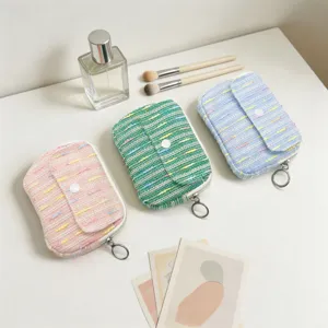 Tweed flap coin purses in pastel colors arranged with cosmetic props on a white desk.