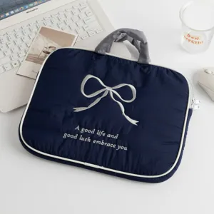 Vista detallada de funda para portátil azul marino con lazo bordado blanco.