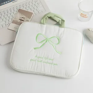 Vista detallada de funda acolchada blanca para portátil con diseño de lazo bordado verde y asa