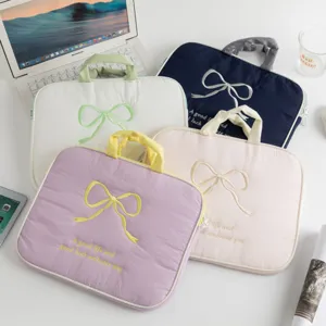 Fundas para portátil con lazo bordado en colores pastel sobre un escritorio blanco.