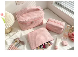 Lot de trois trousses de maquillage en seersucker rayé rose avec accessoires de beauté.