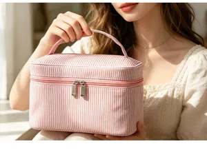Gros plan d'une trousse de maquillage en seersucker à rayures roses tenue par la main.