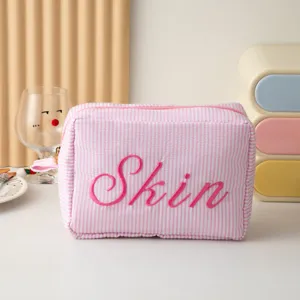 Détail rapproché d'une trousse à maquillage à rayures roses et blanches brodée Skin rose
