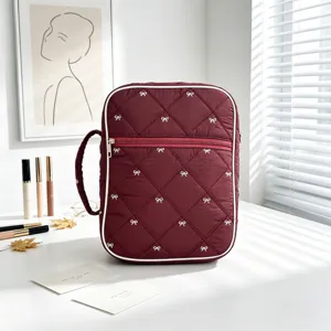 Bolsa acolchada granate para libros con lazos blancos en un escritorio con luz natural.