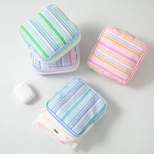 Detail view of striped seersucker pouch storing sanitary napkin and earbuds