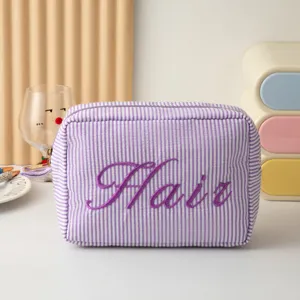 Vue détaillée montrant la texture et la broderie Hair sur une trousse de maquillage à rayures