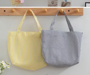 Detail of two striped canvas tote bags in yellow and black hanging on wooden hooks.