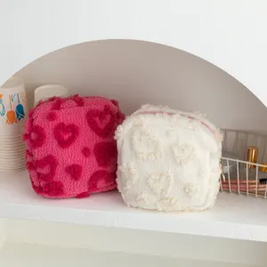 Twee pluche make-uptassen met hartjespatroon op een minimalistische witte plank.