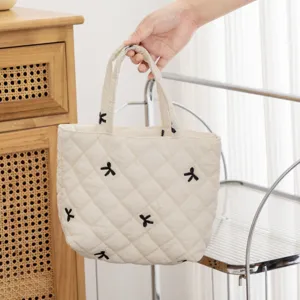 Detalle de un bolso acolchado crema con elegantes motivos de lazos bordados en negro